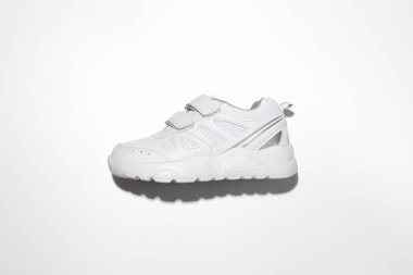 Beyaz bir çocuk, beyaz bir arka planda izole edilmiş sert gölgeler ve cırt cırt cırtlı bağcıklı spor ayakkabıları ile yatıyordu.