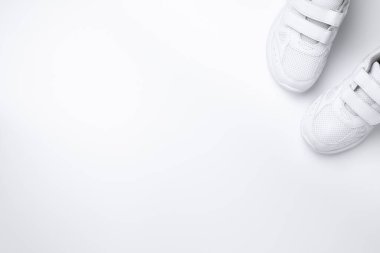 Düz bir zeminde iki beyaz spor ayakkabı kısmen beyaz bir arkaplan üzerinde izole metin için boş alan ile köşede yer almaktadır