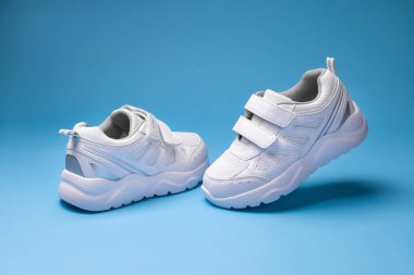 Ön manzara cırt cırtlı çocuk ayakkabıları, havada uçan bir spor ayakkabı ve mavi arka planda tek başına yerde duran bir spor ayakkabı.