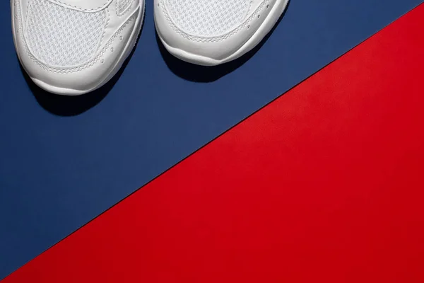 Parte frontal plana de zapatillas blancas con duras sombras de verano sobre un fondo moderno con una separación diagonal de rojo y azul —  Fotos de Stock