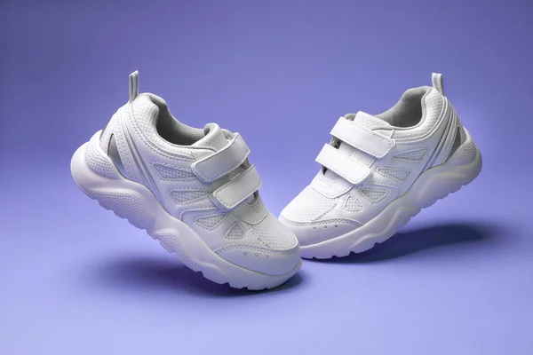 Side view white unisex sneakers with velcro fly in the air toes to each other isolated on purple background — Stock Photo, Image