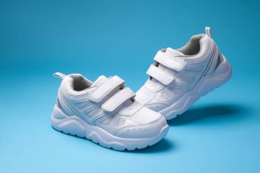 İki beyaz çocuk ayakkabısı ve cırt cırtlı bağcıklar. Çocukların ayakkabıları için, mavi arka planda izole edilmiş.