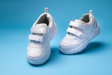 mavi arka planda tek başına yürüyen beyaz koşu ayakkabıları.