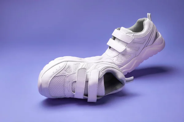 Две белые детские кроссовки с липучками для легкой детской обуви, изолированные на фиолетовом фоне — стоковое фото