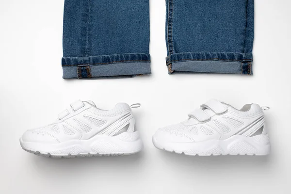 Flat ligning av en mann eller kvinne som går ut av to hvite unisex barnesko og den nederste kanten av jeans isolert på hvit bakgrunn – stockfoto