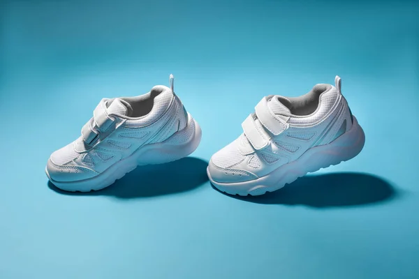 Twee witte kind vliegen in de lucht sneakers simuleren lopen geïsoleerd op een blauwe achtergrond — Stockfoto