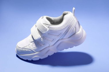 Mor arka planda izole edilmiş bir yürüyüş simülasyonu yapan cırt cırtlı bağcıklı uçan beyaz çocuk ayakkabısı.