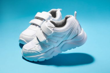 Mavi arka planda izole edilmiş cırt cırtlı bağcıklı iki yürüyen beyaz kadın spor ayakkabısı.