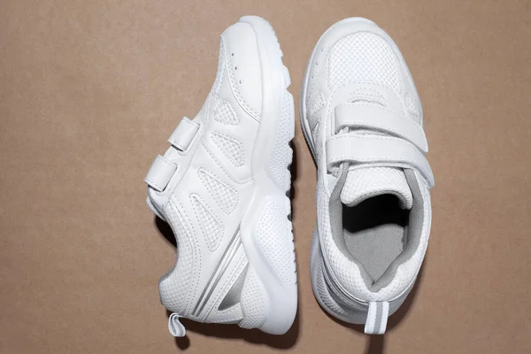 Bovenaanzicht witte kid sneakers met klittenbandsluiting, een sneaker aan de zijkant geïsoleerd op een beige ambachtelijke papieren achtergrond — Stockfoto