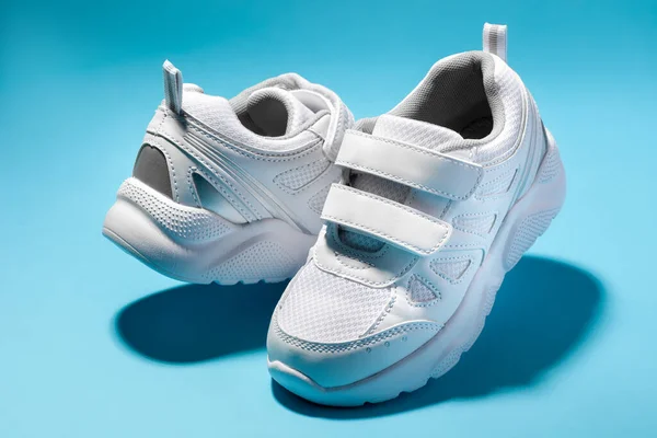 Macro of two white childrens floating sneakers with velcro facing each other isolated on a blue background — Stock Photo, Image