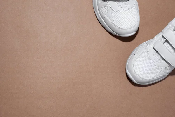 Επίπεδο θέσει δύο λευκά sneakers που βρίσκονται εν μέρει στη γωνία με ελεύθερο χώρο για κείμενο απομονώνονται σε ένα μπεζ φόντο χαρτί χειροτεχνίας — Φωτογραφία Αρχείου