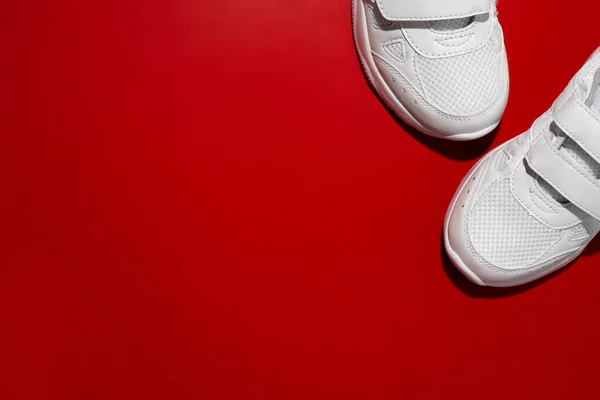 Vista superior a frente de dois tênis esportivos brancos no canto com espaço de cópia isolado em um fundo vermelho com luz dura — Fotografia de Stock
