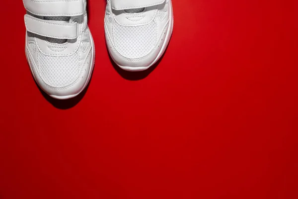 Вид сверху на переднюю часть двух белых спортивных кроссовок в углу с копировальным пространством, изолированным на красном фоне с жестким освещением — стоковое фото