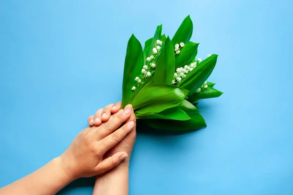 Les mains de la femme tiennent un lis du bouquet de la vallée sur le fond bleu isolé. Concept de fête des mères ou d'été — Photo