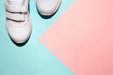 Üst görünüm beyaz unisex spor ayakkabıları köşesinde hassas bir geometrik kağıt üzerinde pembe ve mavi arka plan sert gölgeler, metin için kopyalama alanı