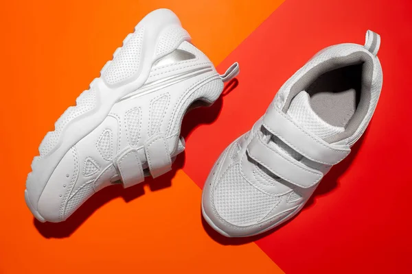 Bovenaanzicht twee witte tiener sneakers met hard licht op een papieren geometrische oranje en rode achtergrond, sneakers als symbool van zomer en vakantie — Stockfoto