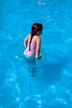 Pembe mayo giymiş bir kızın arka camı otel havuzunda şişirilebilir bir çemberle oynuyor. Suda güvenlik ihlali.