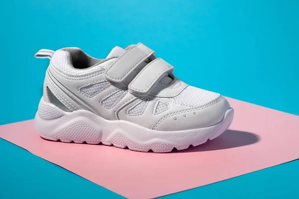 Makro widok z boku jeden biały unisex sneaker z rzepami dla łatwego buta na geometrycznym kwadratowym papierze różowy i niebieski tło z twardym światłem słonecznym — Zdjęcie stockowe