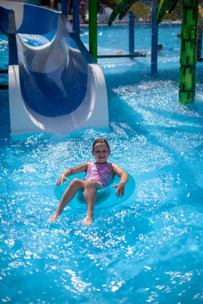 Glücklich lachendes Mädchen im rosafarbenen Badeanzug, das im Familienurlaub auf einem aufblasbaren Kreis in einem Wasserpark schwebt — Stockfoto