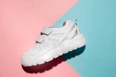 Üst görünüm bir beyaz spor ayakkabı yan tarafında cırt cırtlı bağcıklar kolay ayakkabılar için Geometrik kağıt üzerinde pembe ve mavi arka plan sert ışık