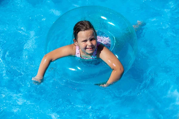 Счастливая улыбчивая девушка, плавающая в прозрачном надувном круге для безопасности на воде в голубом чистом море в летнем путешествии — стоковое фото
