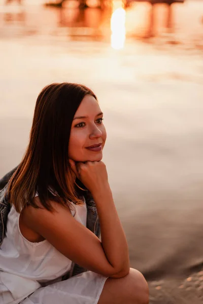 Retrato en el perfil de una hermosa mujer bronceada con el pelo rojo con una mano cerca de su cara admirando la puesta de sol en la orilla del mar —  Fotos de Stock