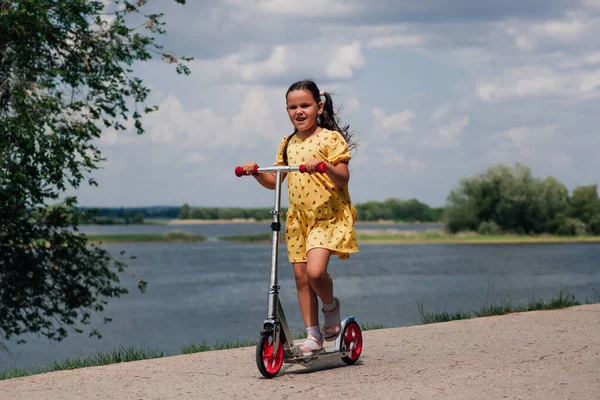 Счастливая, улыбающаяся девушка в желтом платье, катающаяся на скутере, девушка хорошо проводит время и наслаждается семейной прогулкой по реке в летний день — стоковое фото