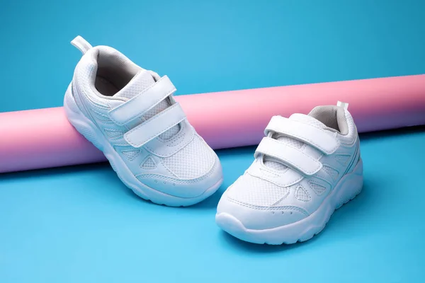 Close-up twee witte vrouw sportschoenen op een roze lange papieren buis op een geometrische blauwe achtergrond in een trendy stijl — Stockfoto