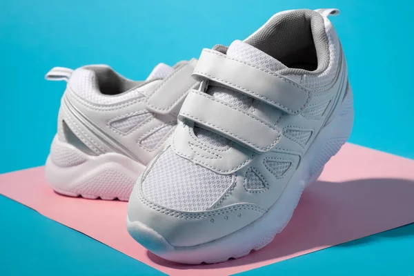 Macro zijaanzicht van twee witte kid sneakers met klittenbandsluiting voor comfortabel schoeisel op een geometrische vierkante papieren roze en blauwe achtergrond met harde schaduwen — Stockfoto