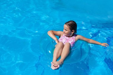 Pembe mayo giyen mutlu bir kız yaz tatilinde otelin havuzunda saydam bir şişme çemberin üzerinde soğuktur.