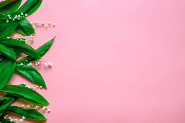Petits bouquets et feuilles vertes de lys de la vallée comme une bordure florale sur la gauche avec espace de copie. Pose plate avec fond rose — Photo