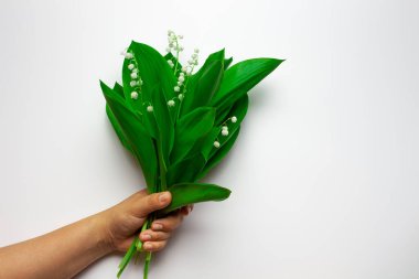 Dişi el, beyaz izole arka planda vadi buketinin zambaklarını tutuyor. Bahar ya da Anneler Günü konsepti