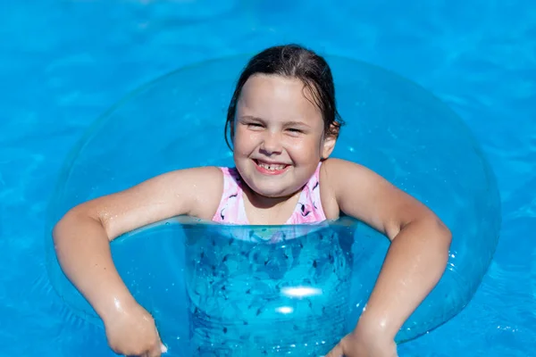 Крупным планом портрет улыбающейся пятилетней девочки, лежащей на поверхности воды на надувном круге, жаркий летний день у моря — стоковое фото