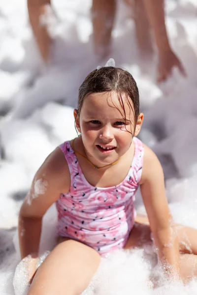Pembe mayo giymiş beyaz bir kız köpük partisinde havuzun kenarında oturmuş iyi vakit geçiriyor. — Stok fotoğraf