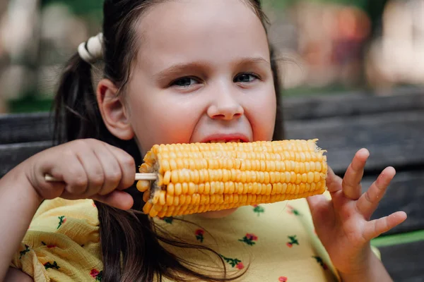 Close-up portrait in detail of a girl biting sweet hot corn on a hiking trip in a summer green forest — Stock Photo, Image