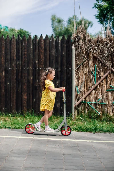 Una bambina di cinque anni guida uno scooter oltre una recinzione di legno in un parco divertimenti durante un fine settimana in famiglia in estate — Foto Stock