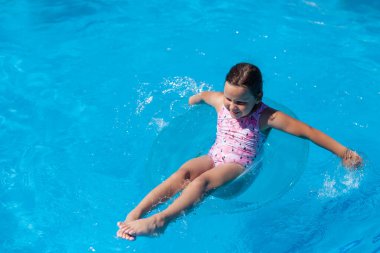 Çekici, uzun boylu bir kız otellerin yüzme havuzunda mavi şeffaf bir şişme dairede yüzüyor ve yazın tadını çıkarıyor.