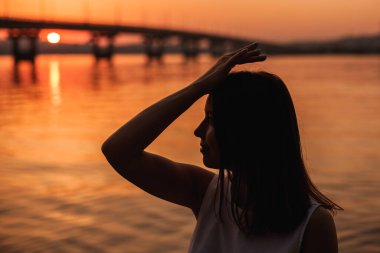 Yakın plan profil silueti, elinde deniz kenarında poz veren bir kız ve gün batımında romantik bir randevuda bir köprü.