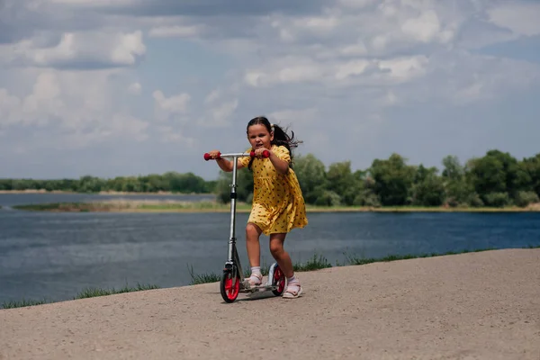 Stile di vita ritratto di una ragazza che guida uno scooter ad alta velocità lungo la riva del fiume, una ragazza con uno scooter come concetto di vacanza in famiglia — Foto Stock