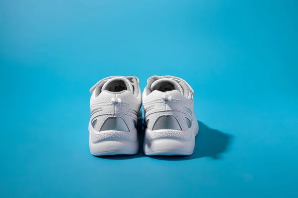 Visão traseira de duas costas ou saltos de tênis branco para crianças com inserções de prata em um fundo de papel azul com sombras duras — Fotografia de Stock