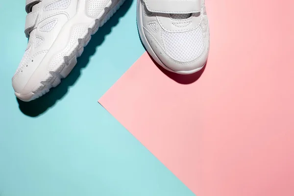 Üst görünüm iki beyaz spor ayakkabı hassas bir geometrik kağıt üzerinde pembe ve mavi arka plan, sert gölgeler, metin için boşluk kopyala — Stok fotoğraf