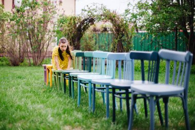 Bir kız dört ayak üstünde tahta sandalyeler üzerinde emekler, yazın doğadaki bir parkta yeşil bir çimenlikte düğün hazırlar.