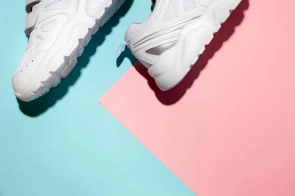 Bovenaanzicht stukjes witte sneakers aan de zijkant op een delicate geometrische papieren roze en blauwe achtergrond met harde schaduwen, kopieer ruimte voor tekst, ochtendtrainingsconcept — Stockfoto