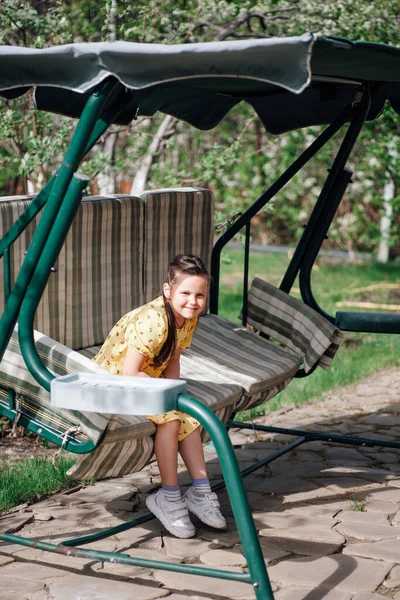 Un niño feliz y sonriente cabalga en un columpio en el patio trasero, el niño se divierte en el columpio en el verano —  Fotos de Stock