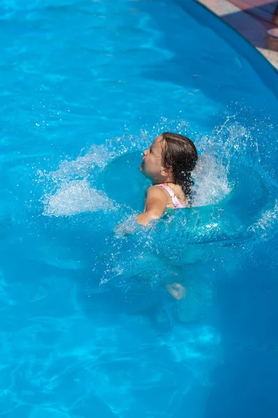Egy ötéves lány beugrik a vízbe a medence széléről, spricceket és vízcseppeket küldözget minden irányba. — Stock Fotó