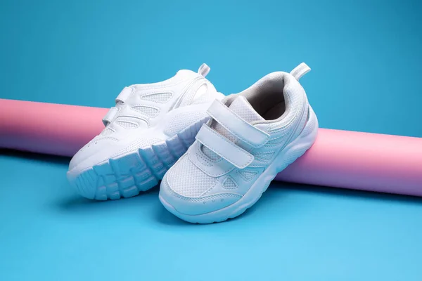 Twee witte tiener sneakers met klittenbandsluiting voor comfortabel schoeisel op een roze lange rol papier op een blauwe achtergrond, een sneaker aan de zijkant — Stockfoto