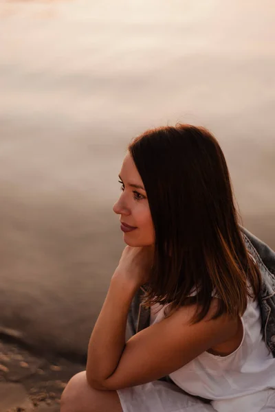 Retrato de perfil de una hermosa joven en el crepúsculo de la puesta del sol con la superficie del mar en el fondo —  Fotos de Stock