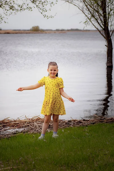 강변의 노란 드레스를 입고 따뜻 한 봄날, 푸른 풀 과 지방 여행을 즐기고 있는 소녀의 모습 — 스톡 사진