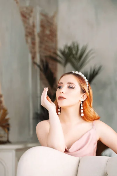 portrait of a glamorous woman in a silk dress with makeup made of mother-of-pearl beads, with long pearl earrings and a headband on her head