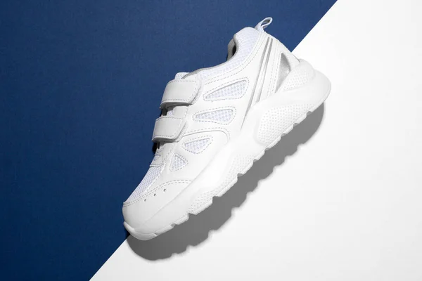 Macro vue de dessus sur le côté une sneaker blanche avec attaches Velcro pour des chaussures faciles sur un fond moderne en papier bleu et blanc avec des ombres d'été dures — Photo